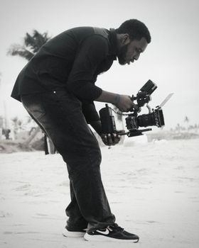 A videographer with camera equipment capturing footage on a sandy beach.