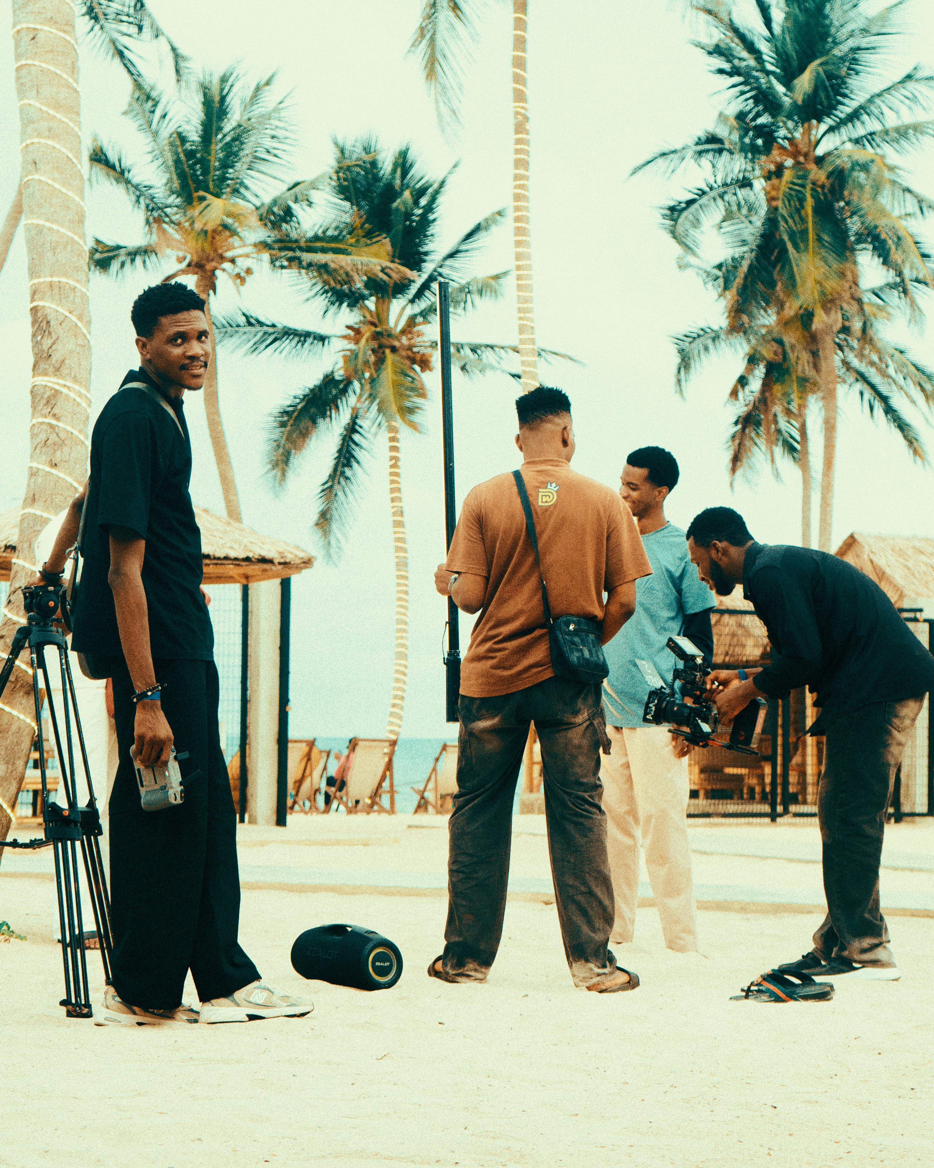 Film crew setting up shoot on a tropical beach with palm trees.