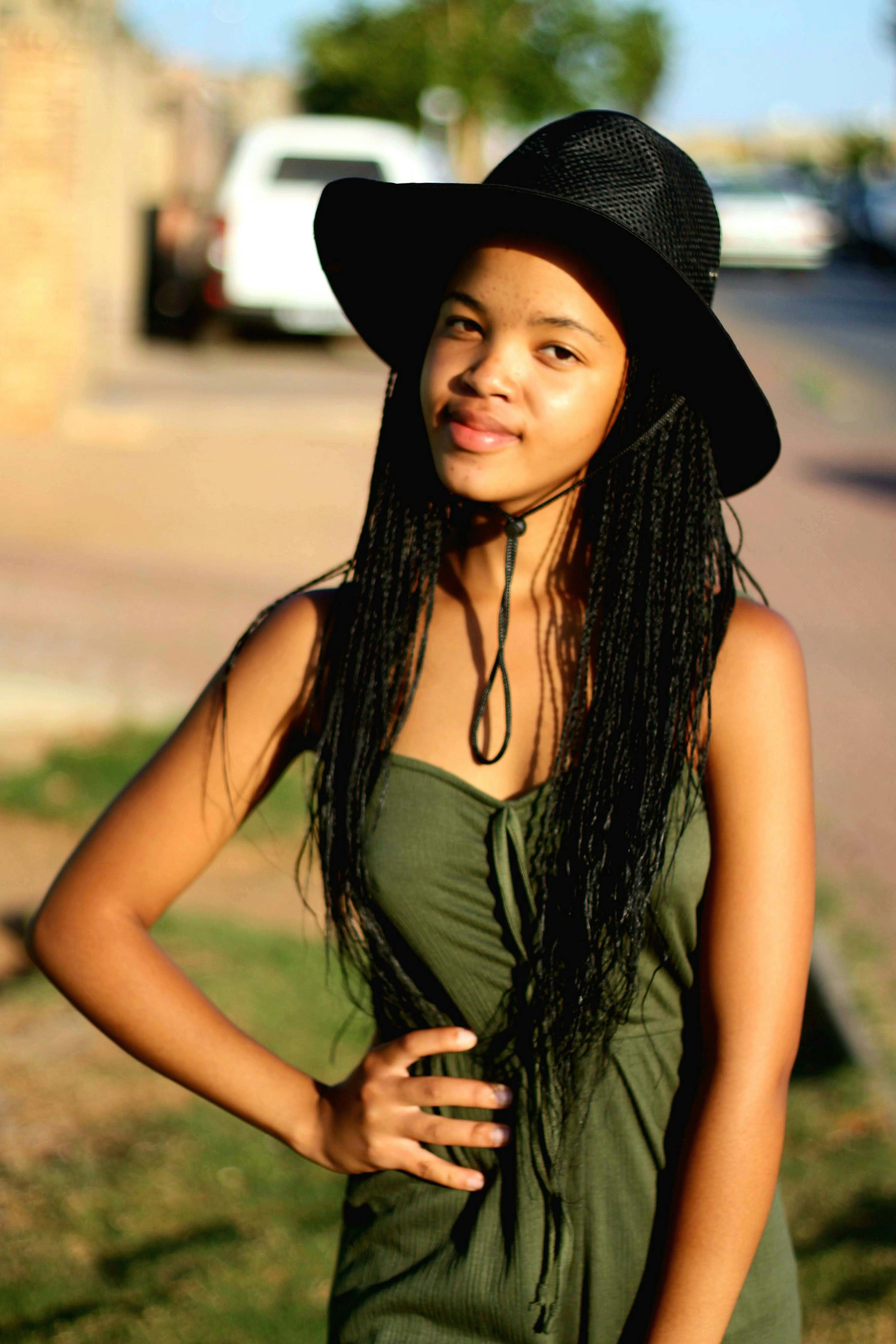 Confident young woman wearing sun hat poses outdoors on a sunny day.