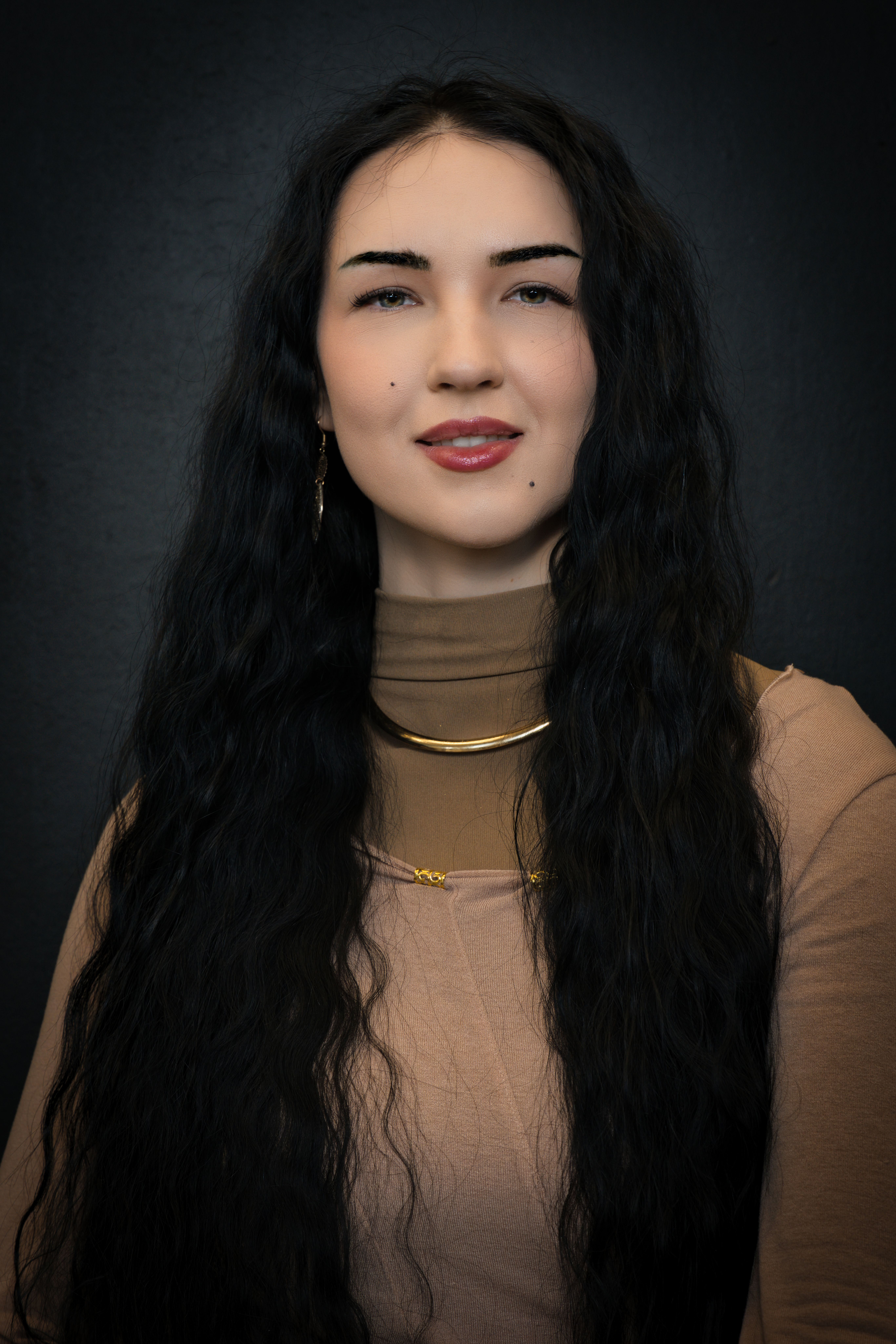 Elegant portrait of a woman with long black hair and gold jewelry, set against a dark backdrop.