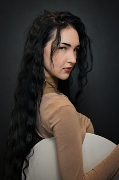 A striking portrait of a woman with long black hair, wearing a beige top against a dark background.
