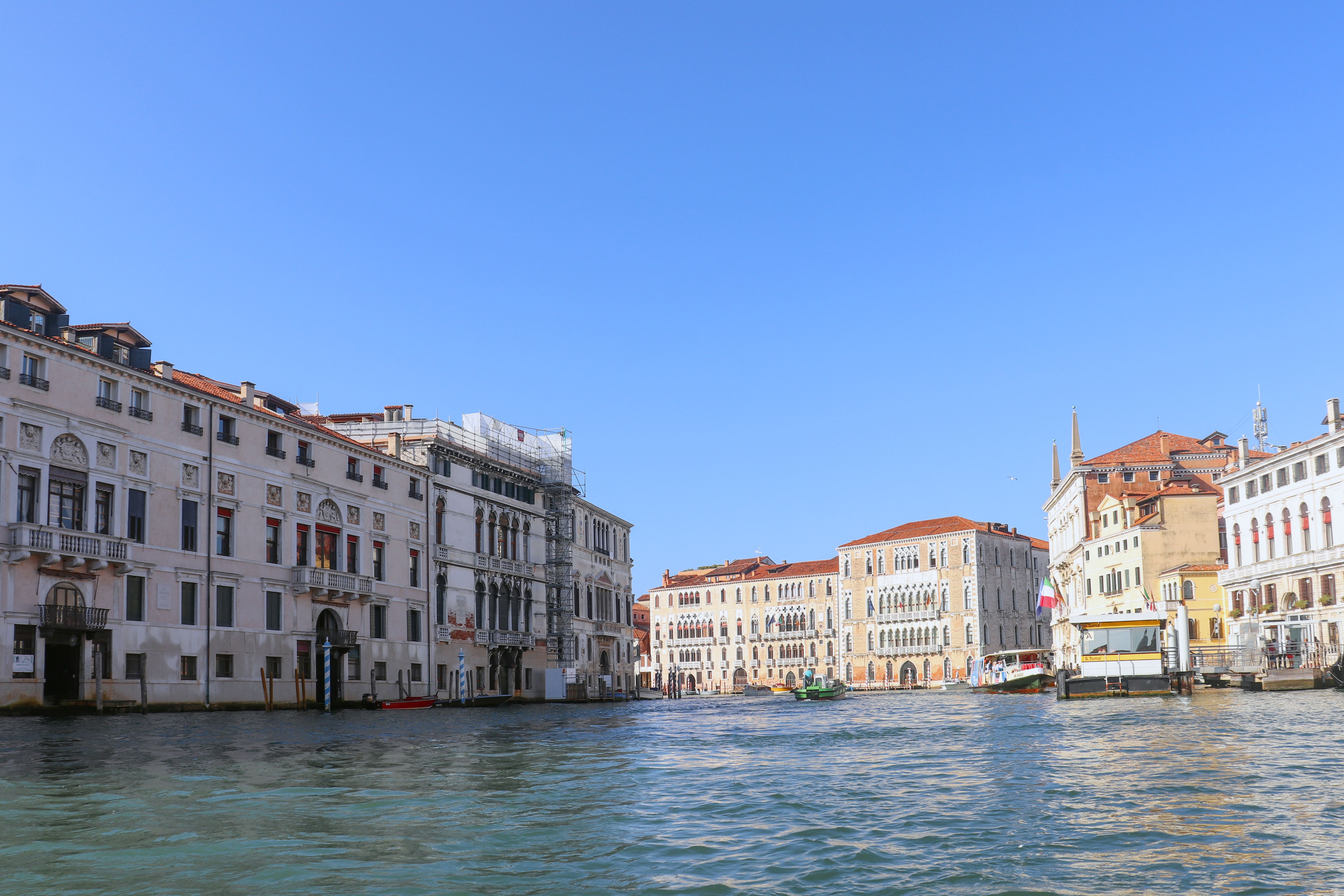 Wide view of the Grand Canal's historic architecture in Venice under a clear blue sky.