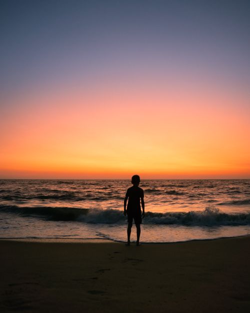 Free A serene silhouette of a person on a beach in India with a vibrant sunset sky. Stock Photo