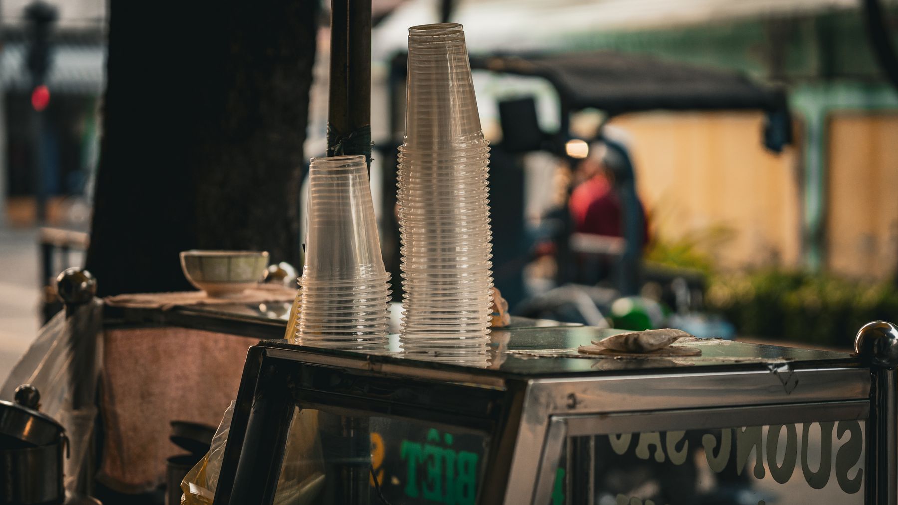 Street vendor cart in Ho Chi Minh City with stacks of plastic cups and bustling street in the background.