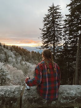 一个穿着格子衬衫的人坐在岩壁上，欣赏着山上美丽的日落景色