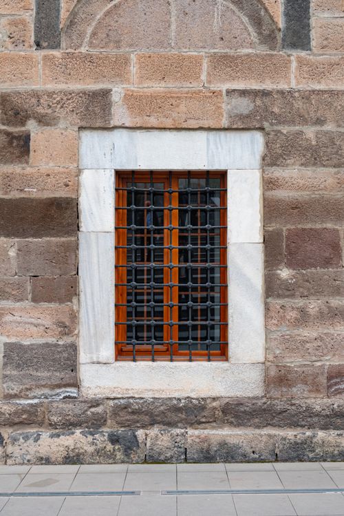 Free A detailed view of a historic stone wall featuring a wooden window with iron grills, showcasing architectural design. Stock Photo