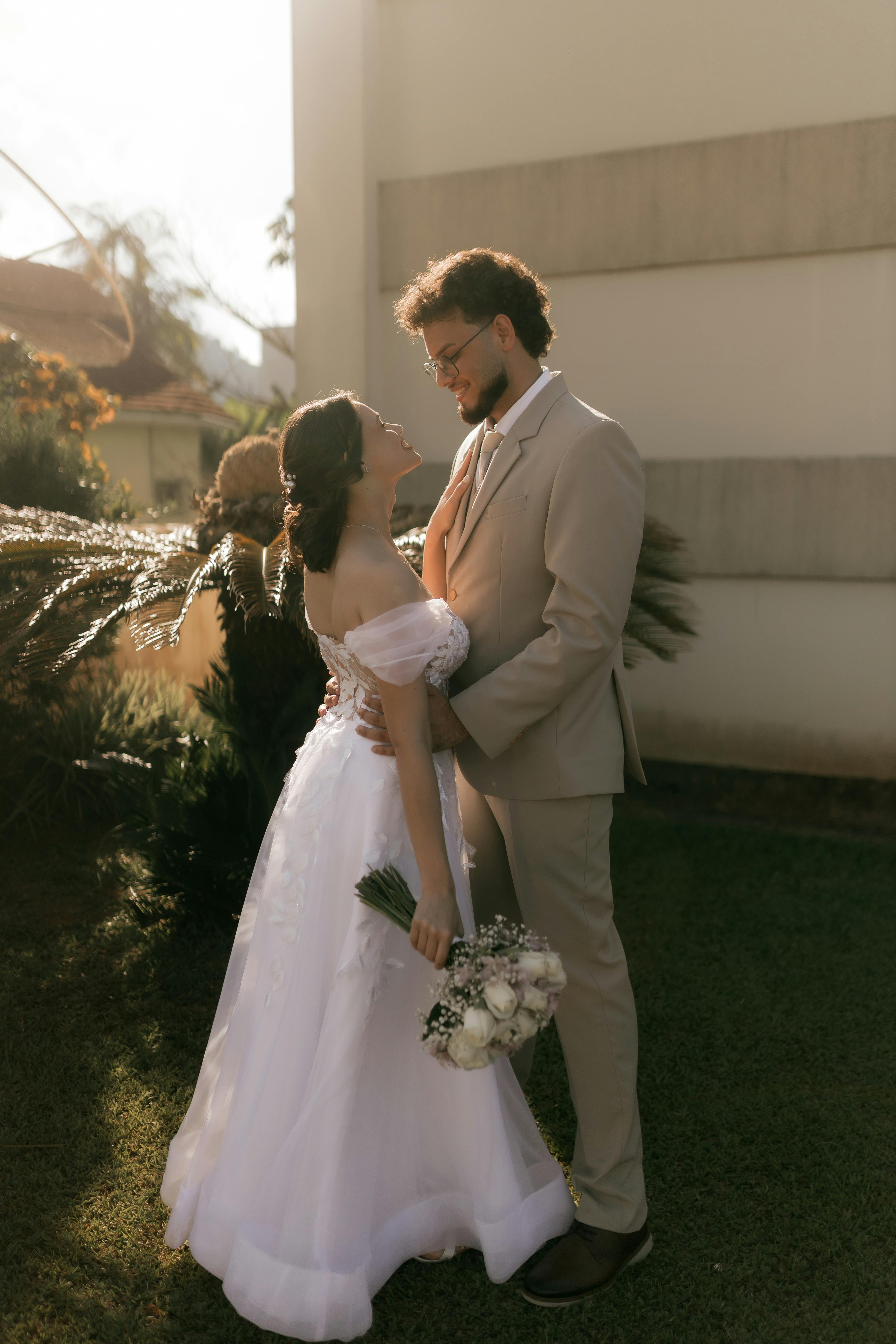 Elegant couple shares romantic moment outdoors in their wedding attire under warm sunlight.