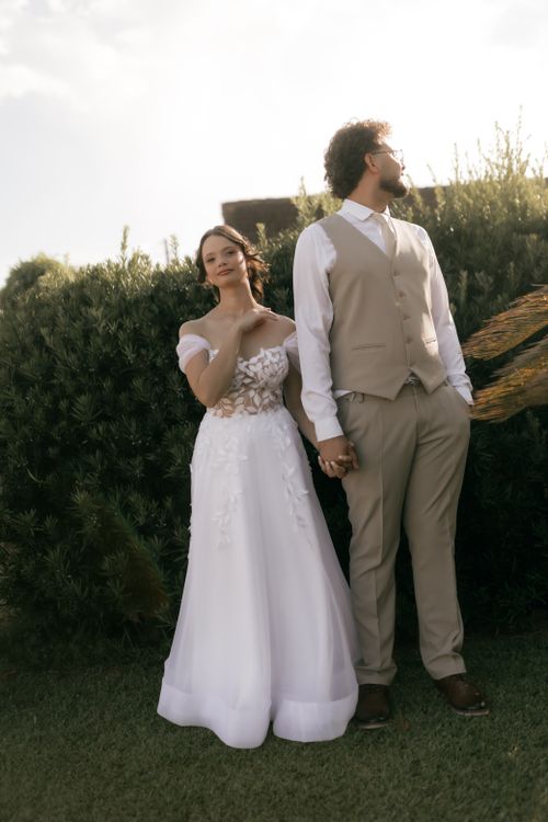 Free Beautiful bride and groom holding hands in an outdoor setting, dressed elegantly for their wedding day. Stock Photo