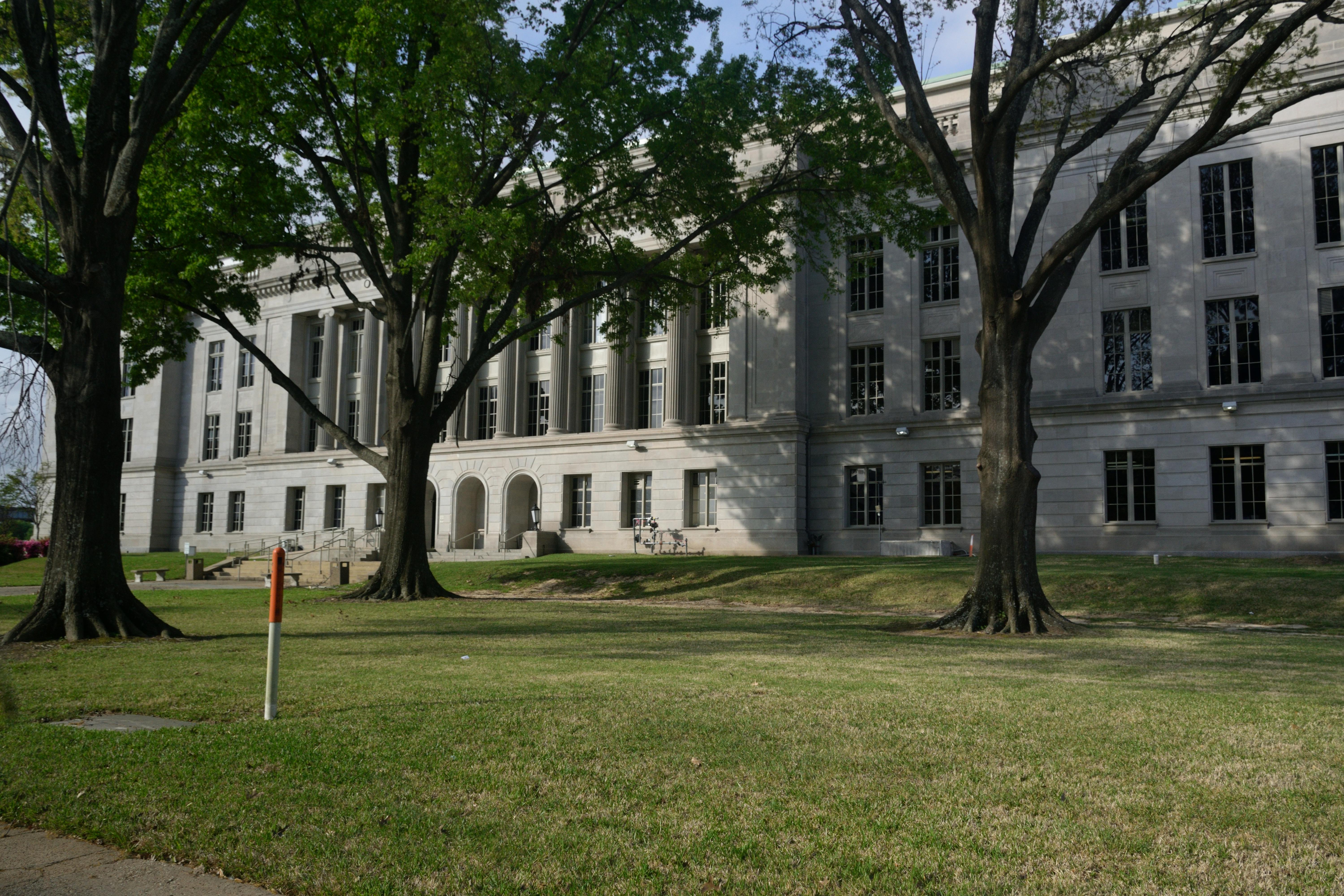 A classic facade of a historic building framed by large trees and lush green lawn.
