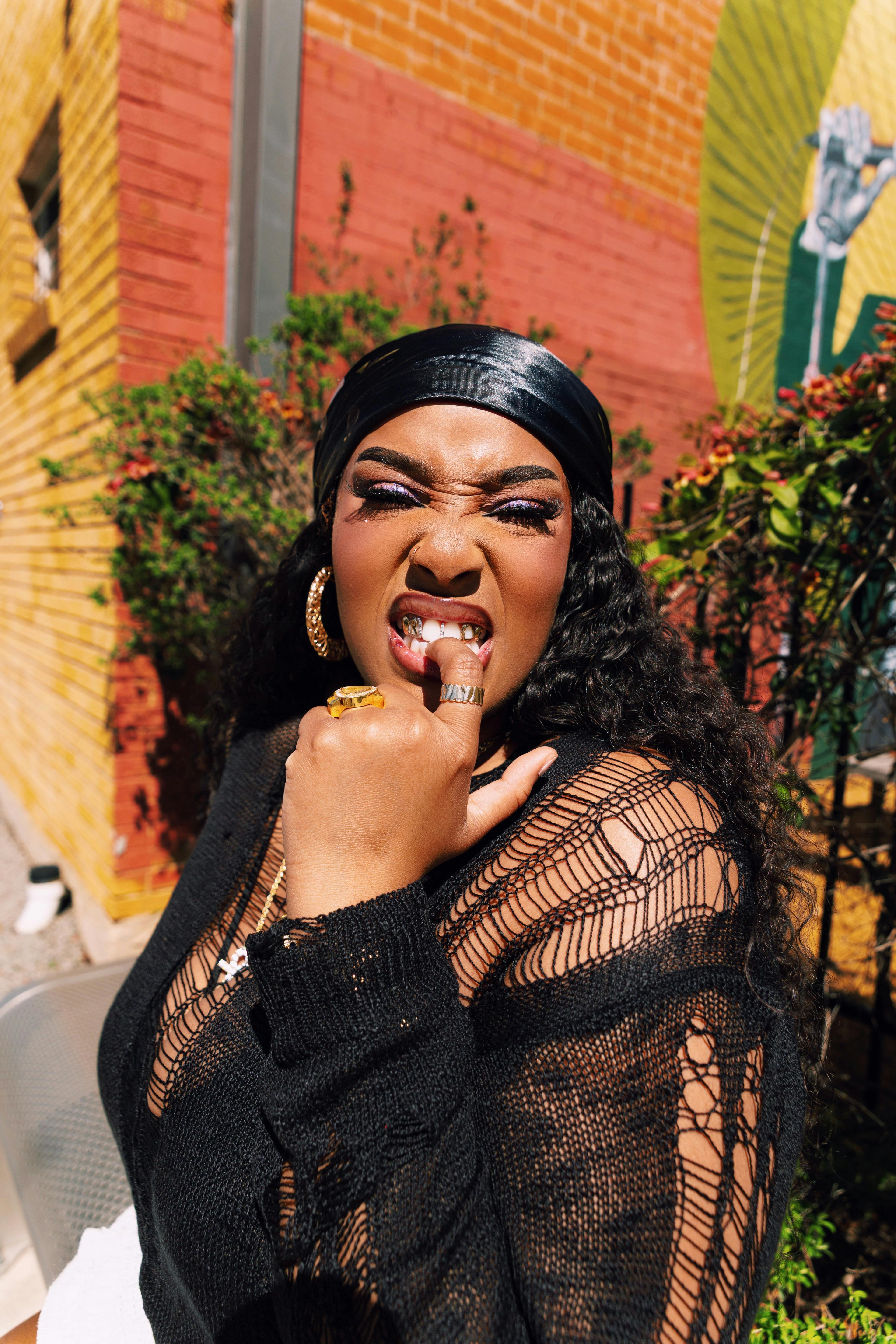 A woman displaying a fierce gesture and stylish attire in a vibrant urban setting, exuding confidence and strength.