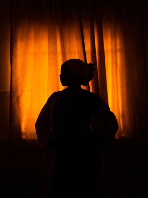 Free Silhouette of a woman in front of glowing orange curtains, creating a dramatic ambiance. Stock Photo