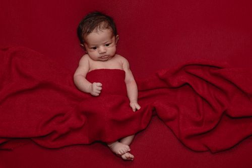 Free Adorable newborn baby wrapped in a red blanket, lying on red fabric. Stock Photo