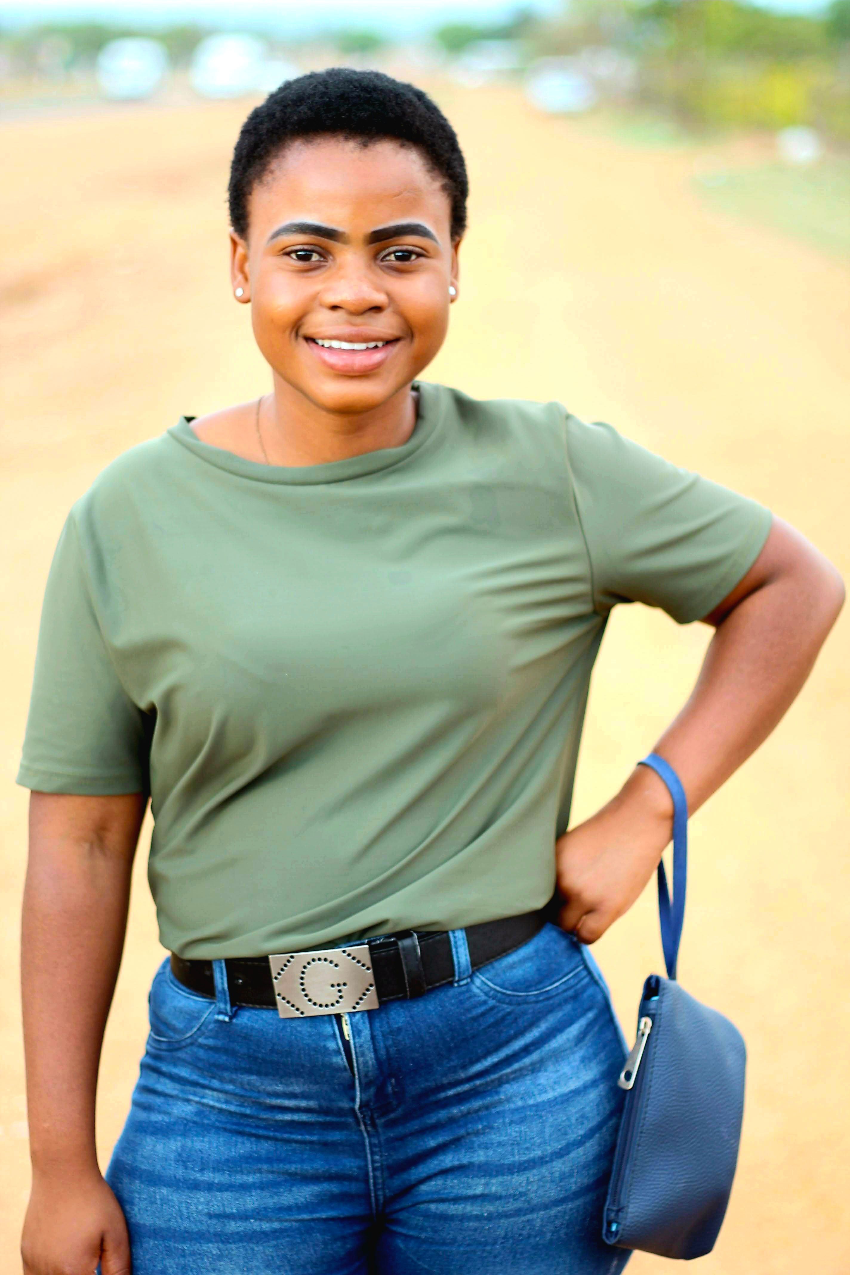 Young woman smiling in casual outfit with green top and blue jeans outdoors.