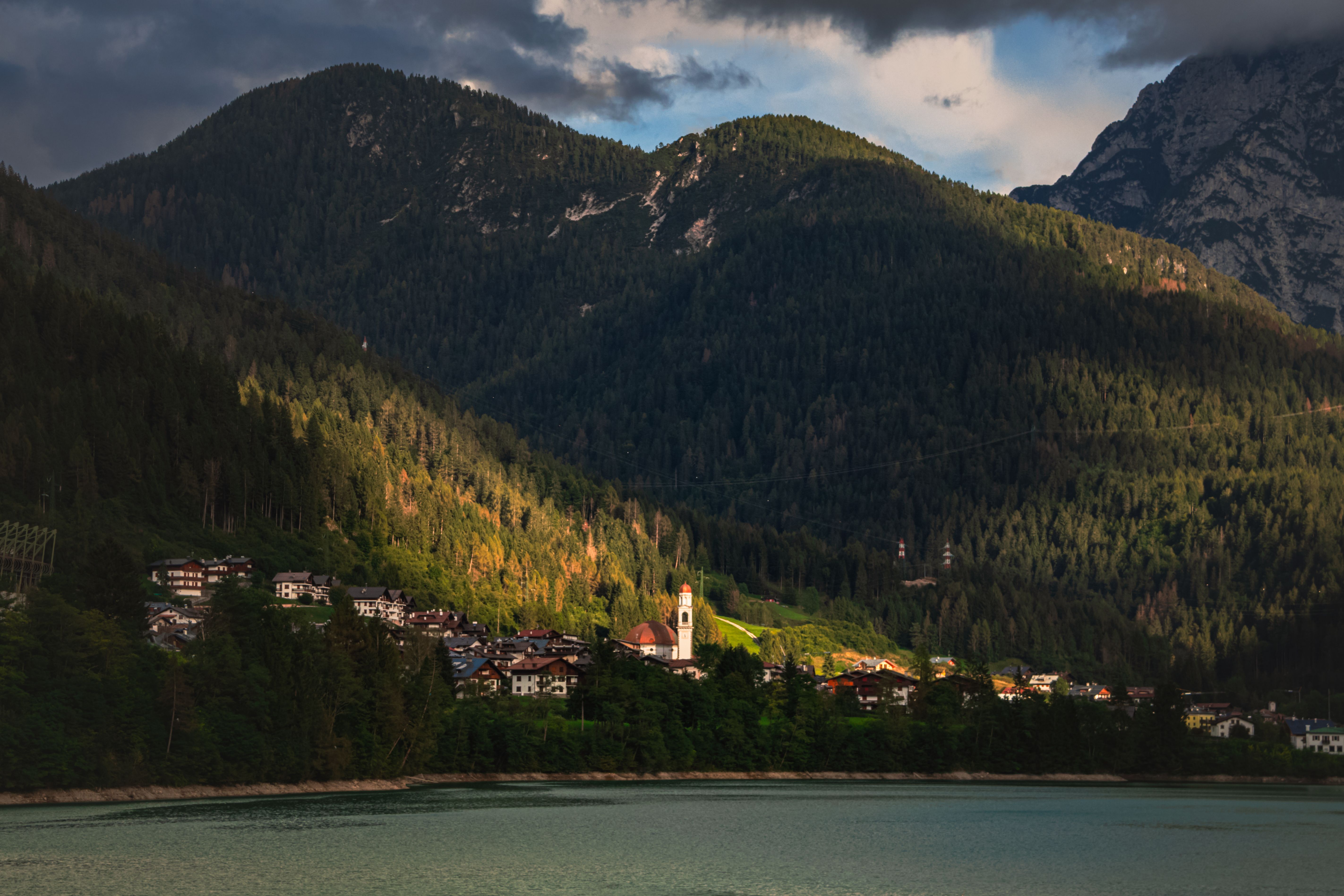 Scenic view of a tranquil village nestled in the Italian Alps, surrounded by lush forests and mountains at dusk.