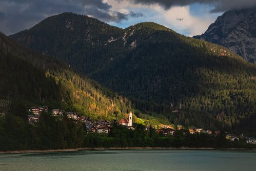 Scenic view of a tranquil village nestled in the Italian Alps, surrounded by lush forests and mountains at dusk.