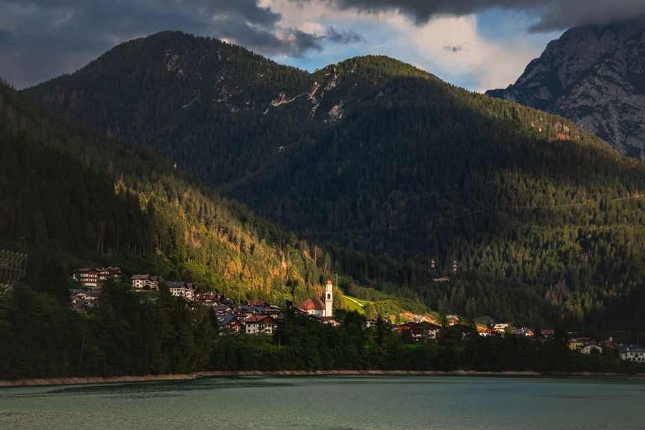 Scenic view of a tranquil village nestled in the Italian Alps, surrounded by lush forests and mountains at dusk.