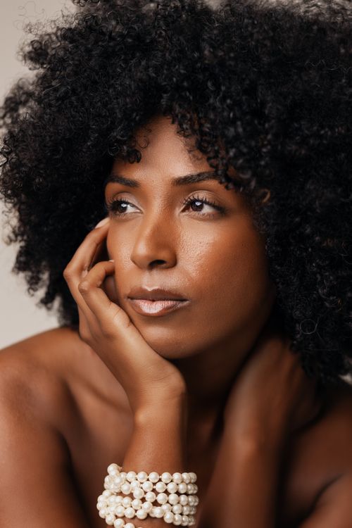 Free Striking portrait of a woman with curly hair adorned with pearl bracelets. Stock Photo