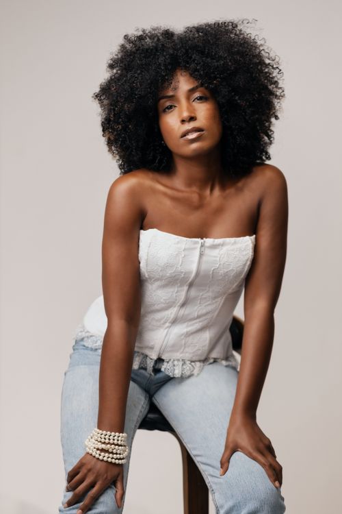 Free Portrait of a confident woman with curly hair wearing a white top and jeans. Stock Photo