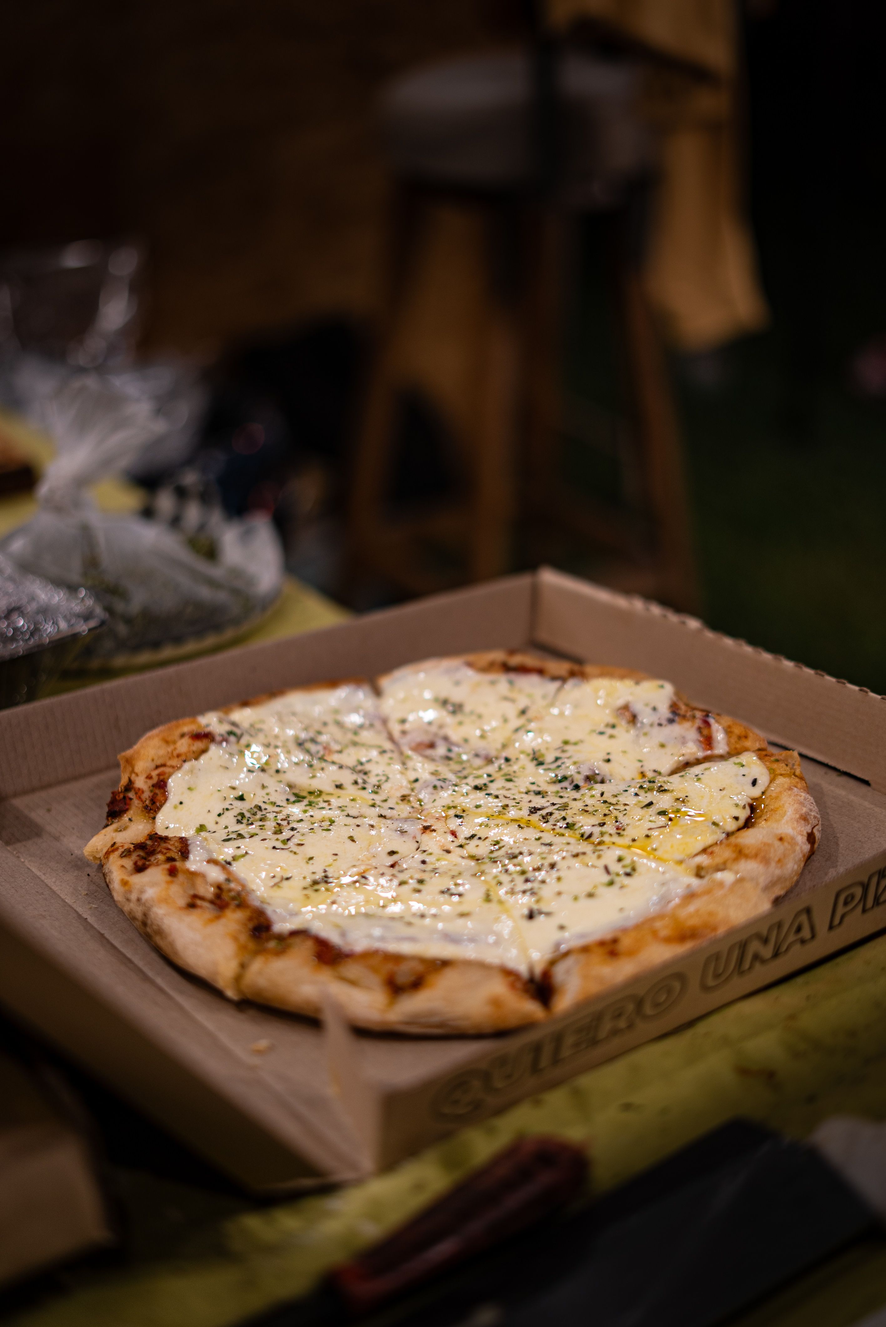 Close-up of a cheesy pizza in a cardboard box on a table indoors, perfect for food promotions.