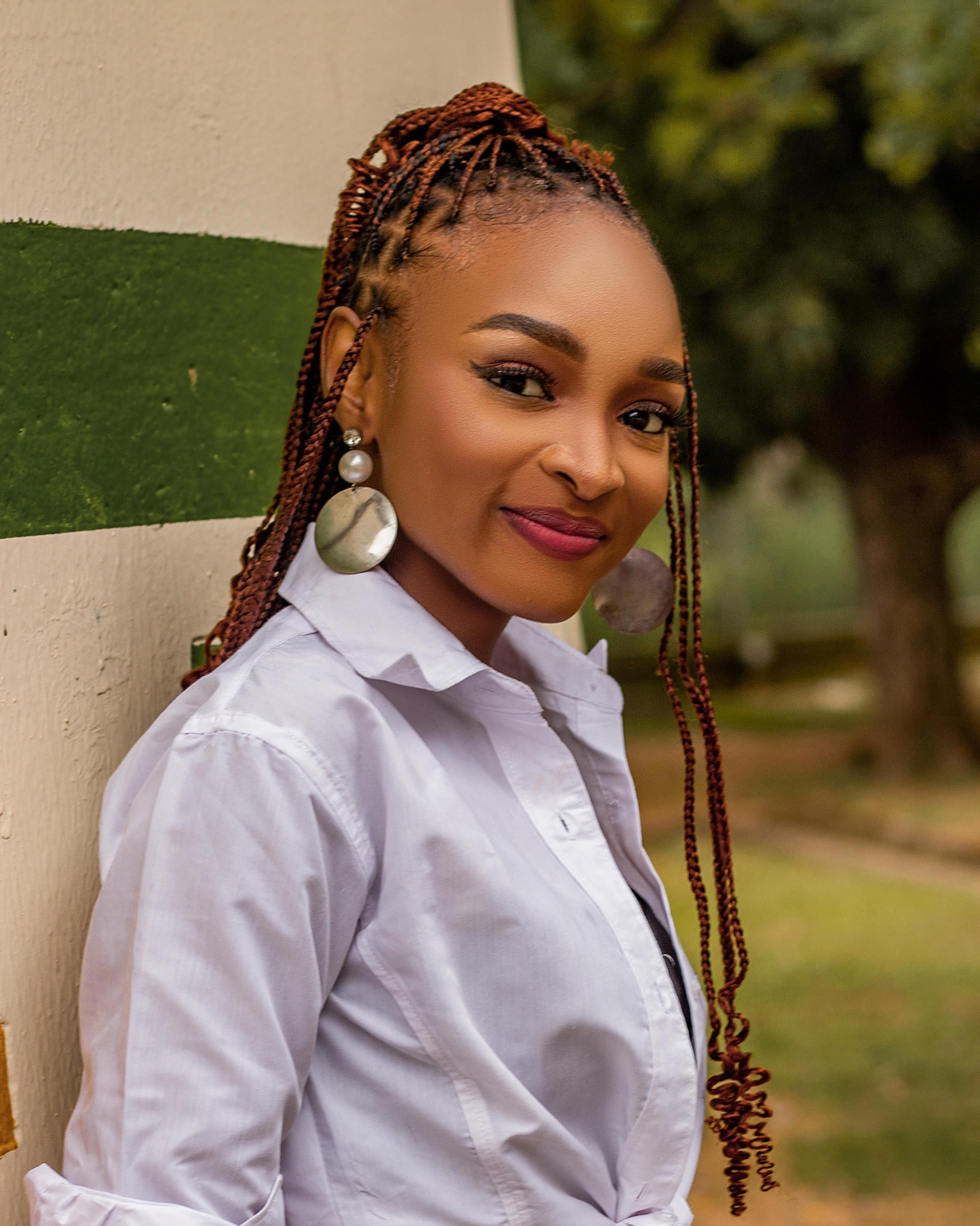 A confident young woman in a white blouse stands outdoors, exuding grace and elegance.
