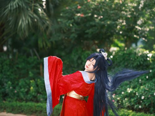 Free A person wearing a traditional red Asian robe poses elegantly outdoors in a lush green garden. Stock Photo