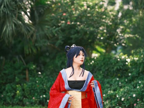 A woman in a vibrant traditional costume posing in a lush green outdoor setting.
