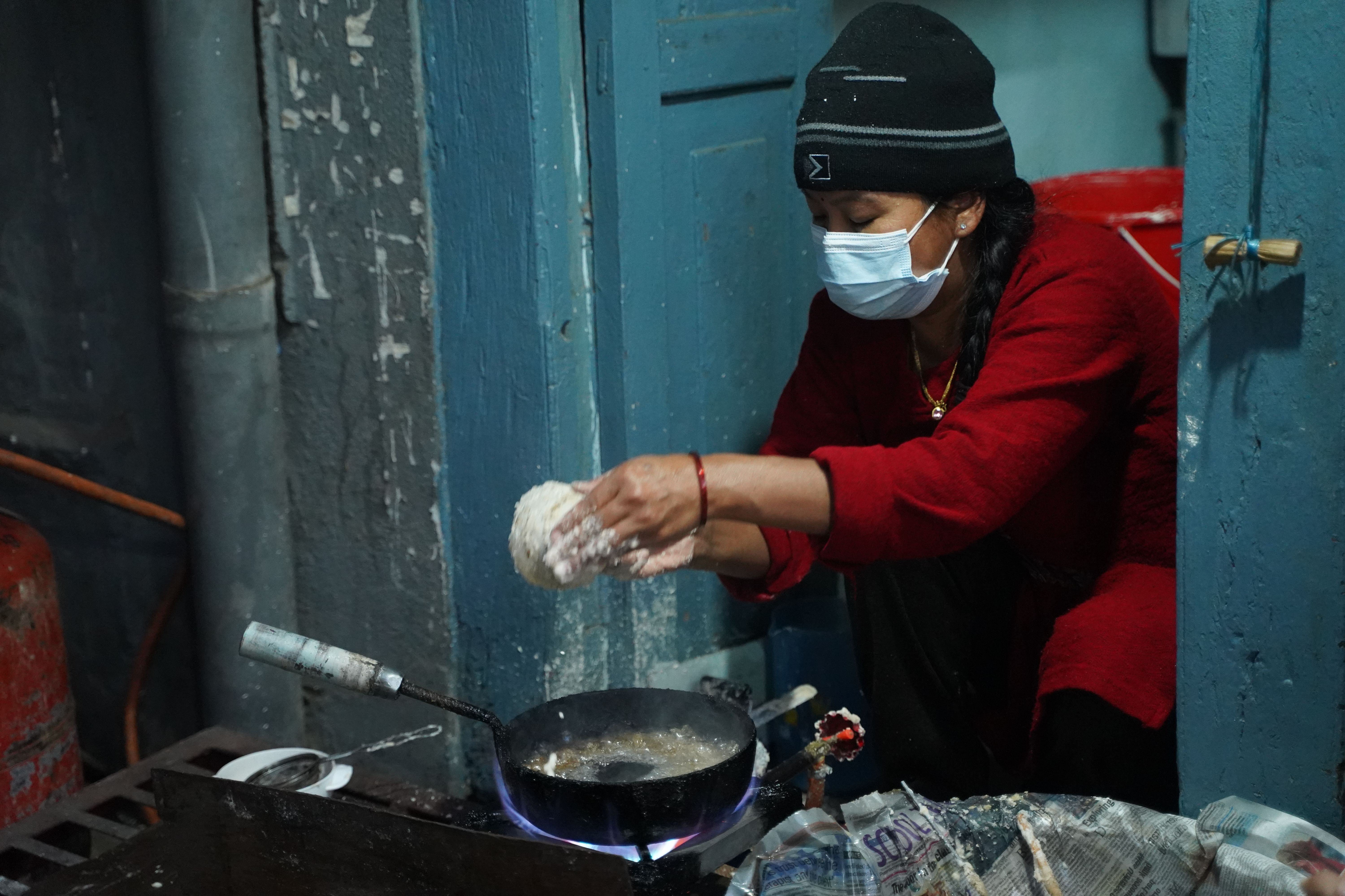 Woman in red cooking indoors, wearing mask for hygiene