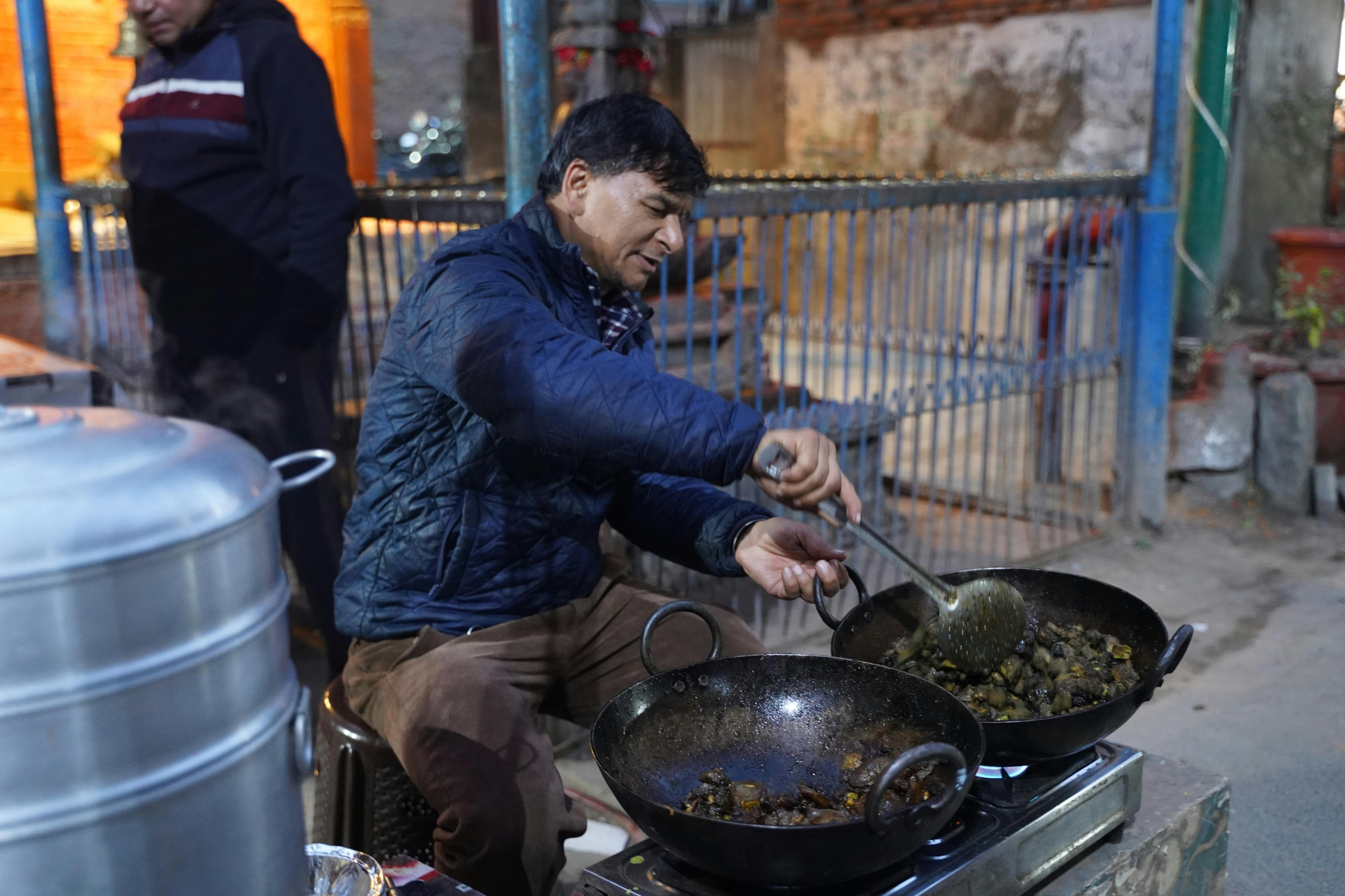 Street food vendor preparing hot dishes in woks at night. Urban outdoor setting.