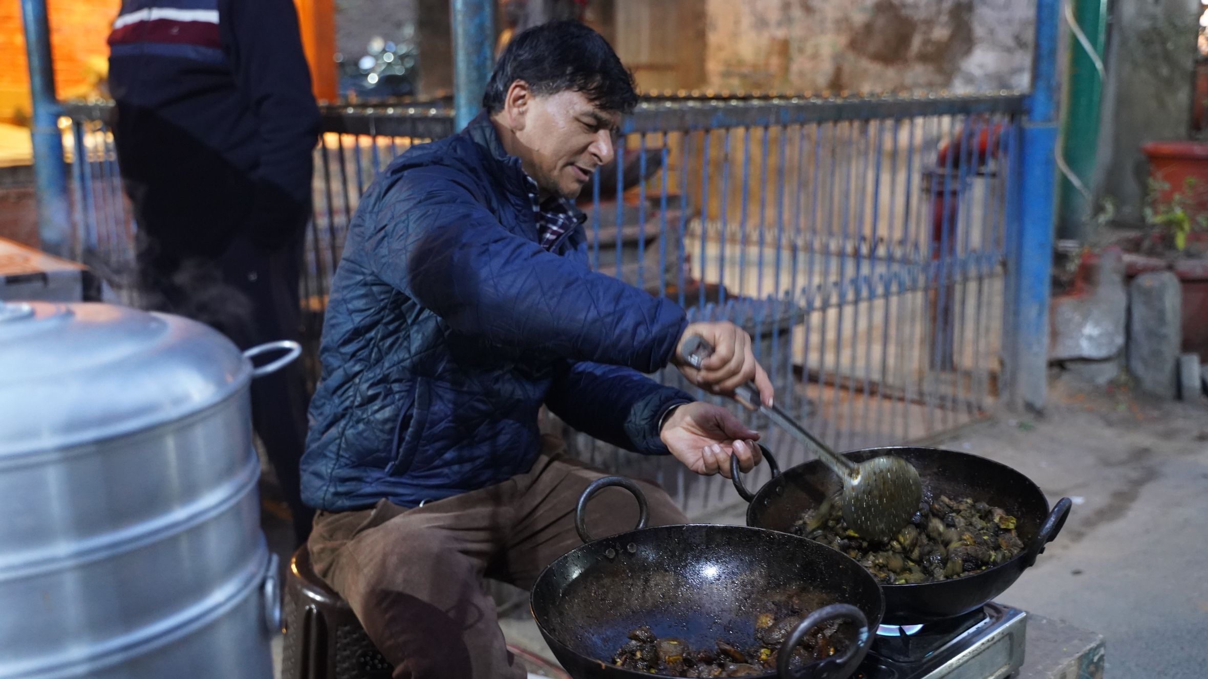 Street food vendor preparing hot dishes in woks at night. Urban outdoor setting.