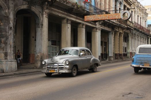 Iconic vintage cars driving past Cuban colonial architecture in Havana.