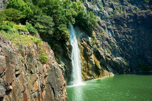 Free A beautiful waterfall cascading down a rocky cliff into a serene green pool. Stock Photo