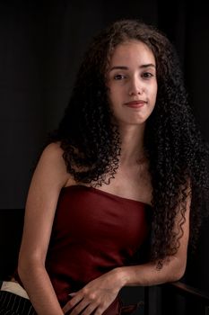 Elegant portrait of a young woman with long curly hair on a dark background.
