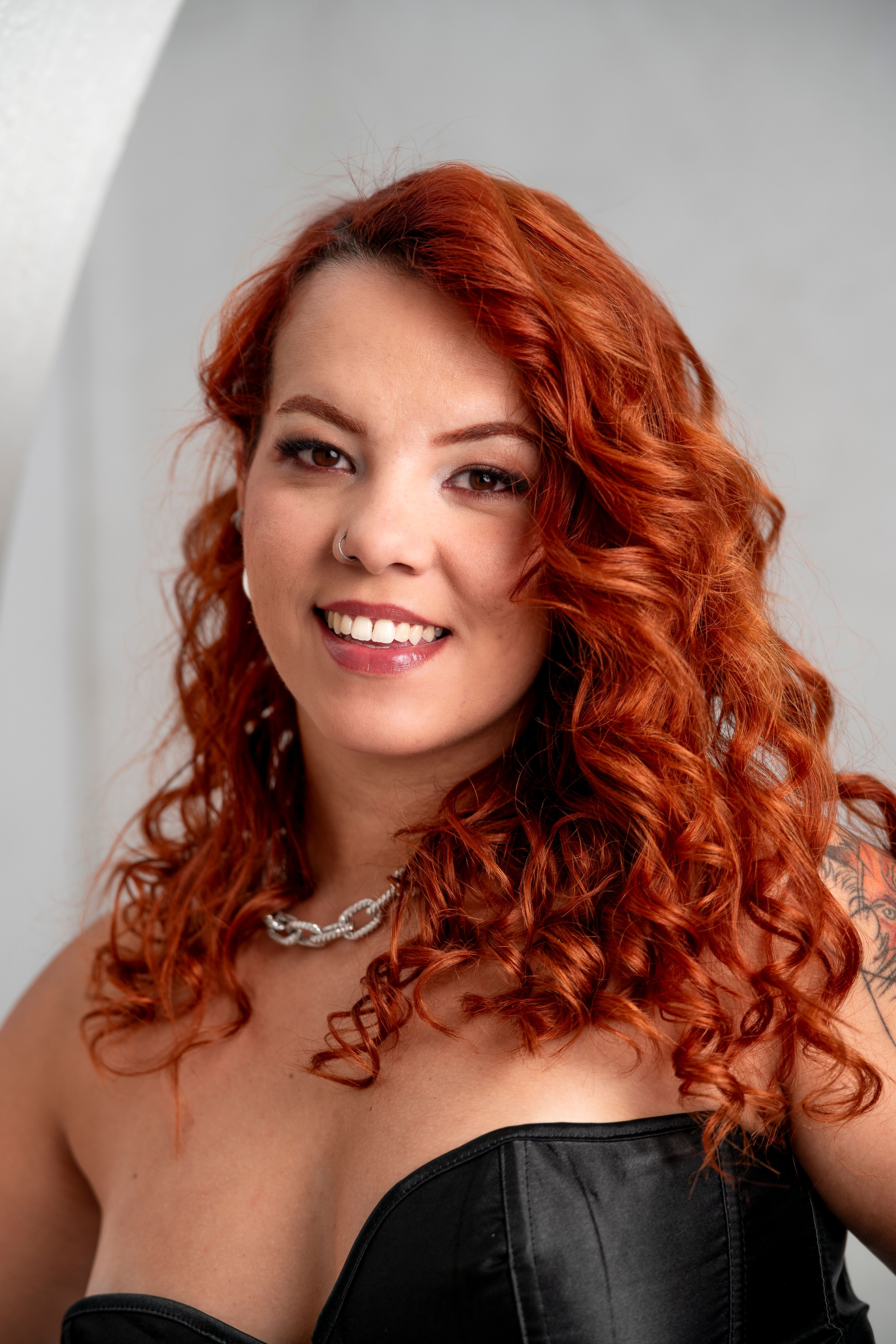 Close-up portrait of a smiling woman with curly red hair and a stylish necklace.