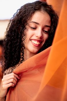 Smiling woman wrapped in soft orange fabric, radiating warmth and happiness.