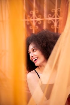 Smiling woman with natural curly hair captured in vibrant orange surroundings creates a cheerful, artistic impression.