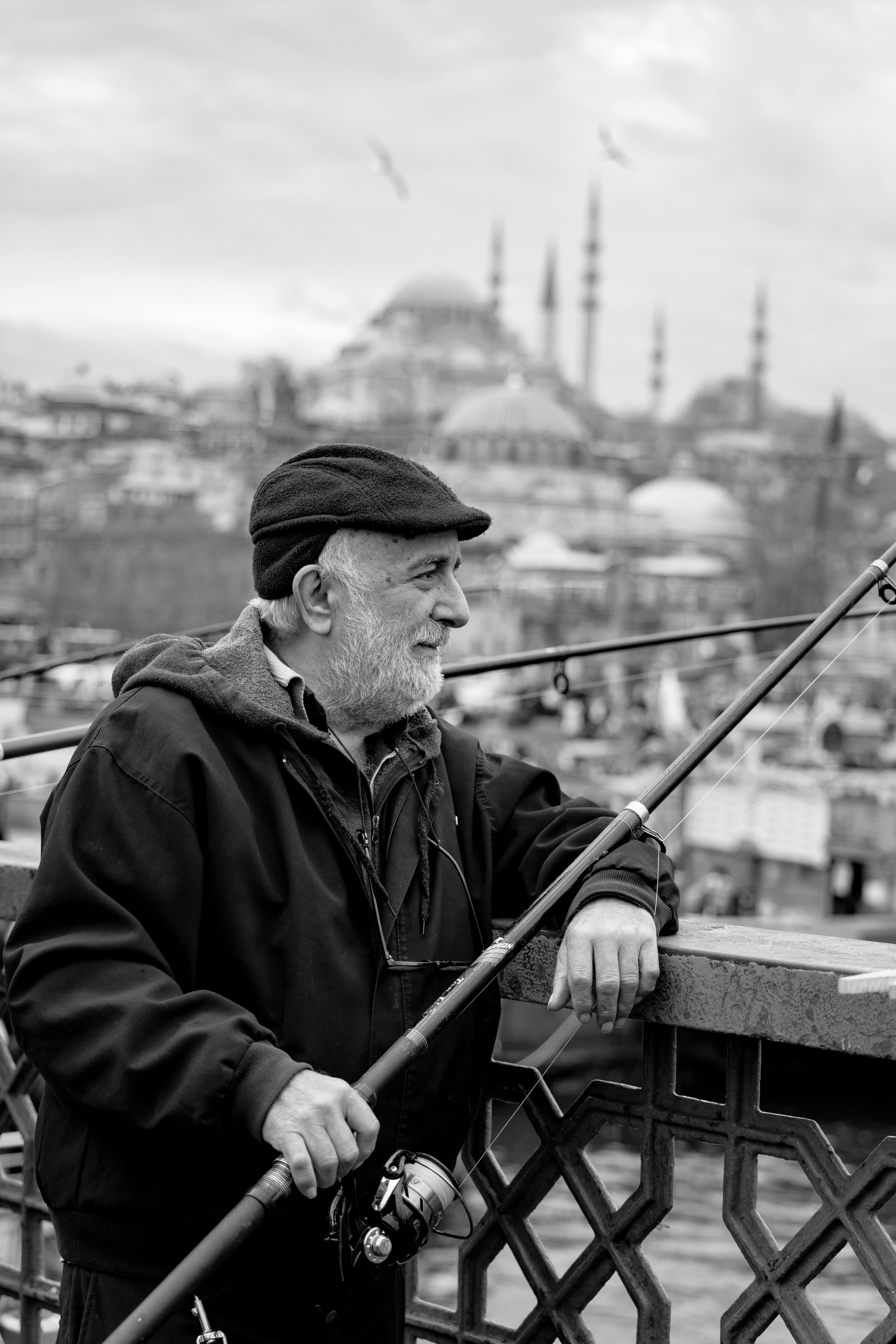Elderly man fishing on Galata Bridge with iconic Istanbul cityscape in view.