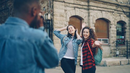 Free Two women posing for a friend's camera in an urban setting. Cheerful and fun vibe. Stock Photo