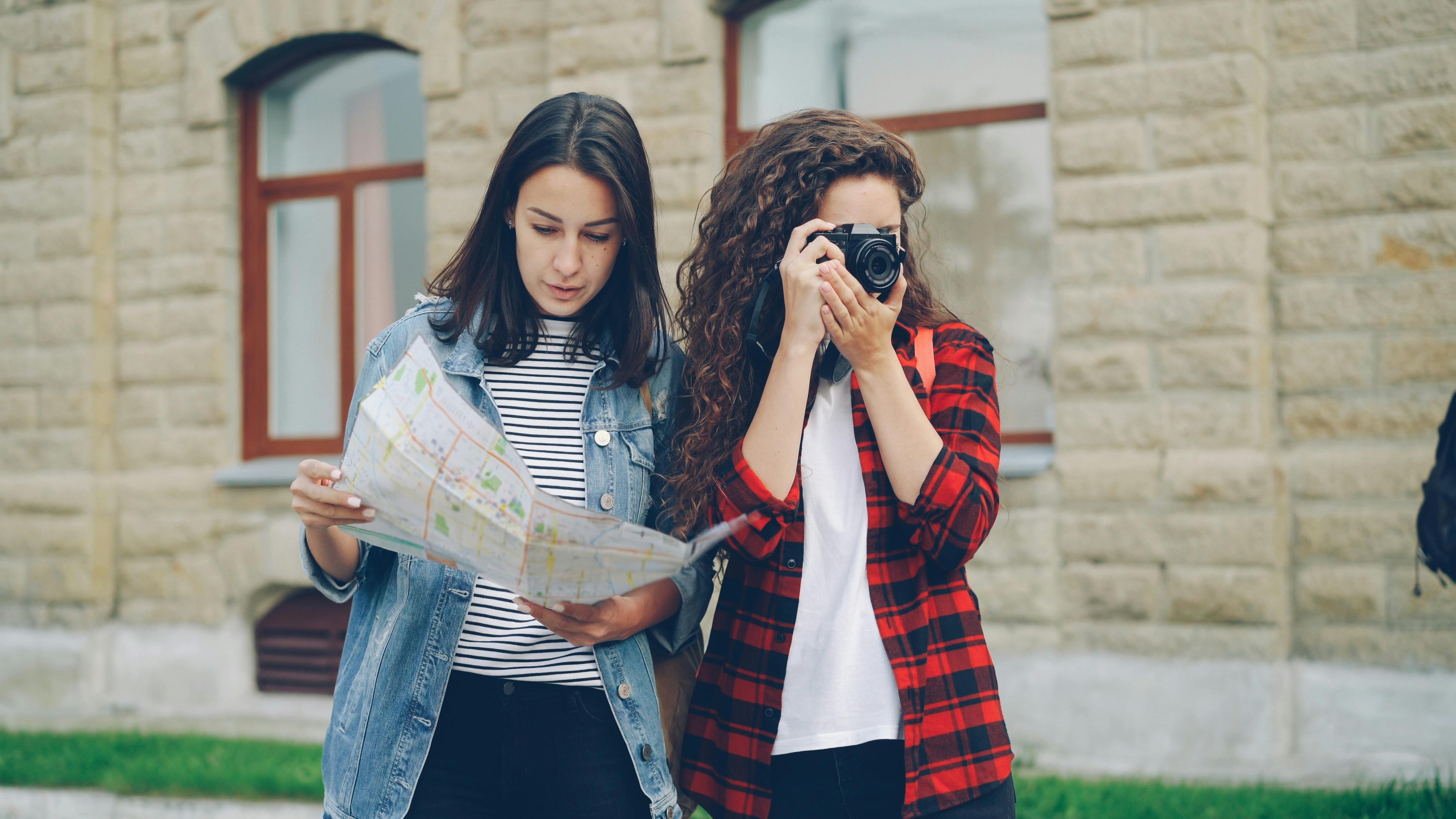 Two young women with a map and camera exploring urban surroundings on a casual outing.