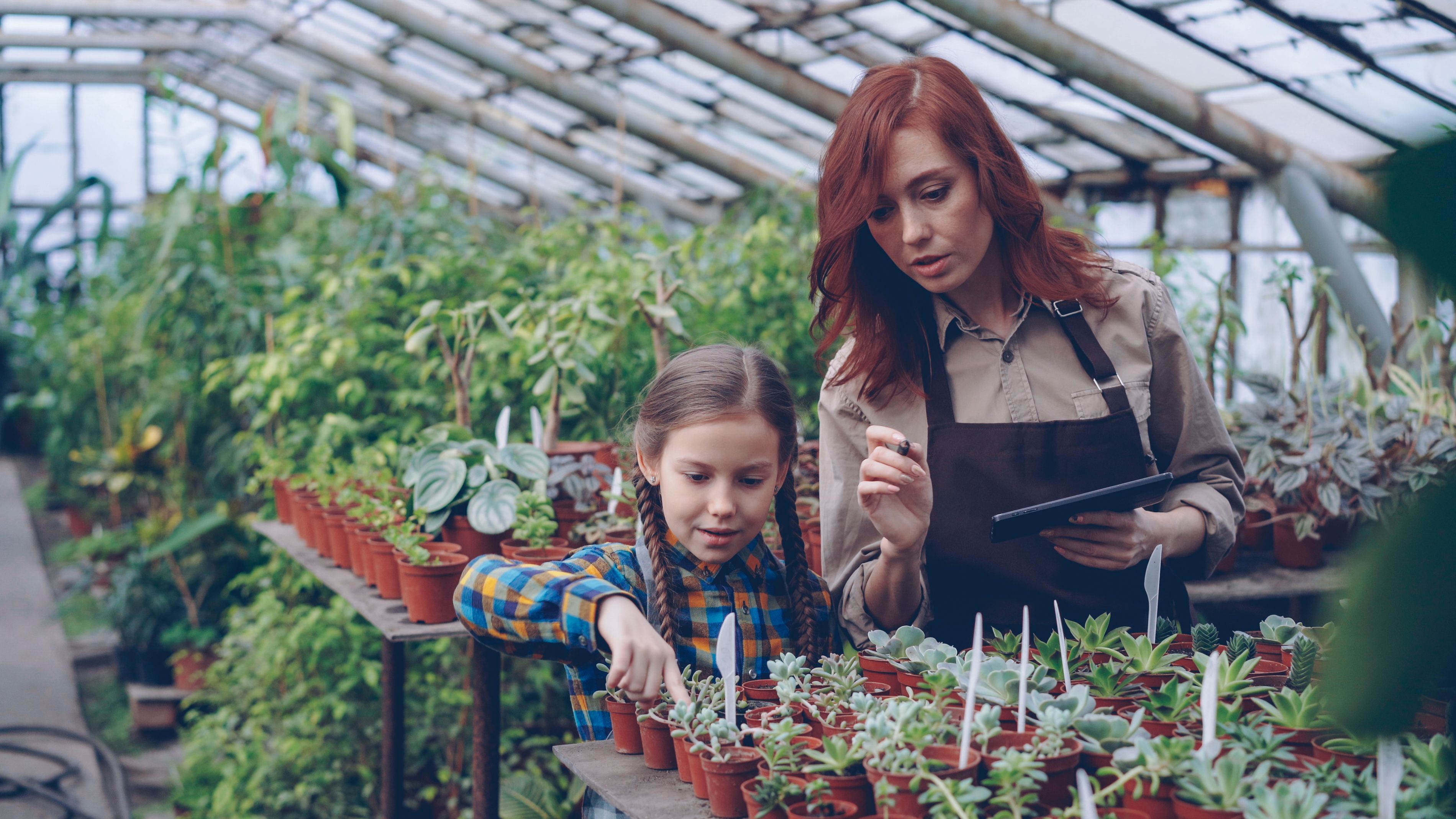 A mother and daughter explore potted plants in a greenhouse.