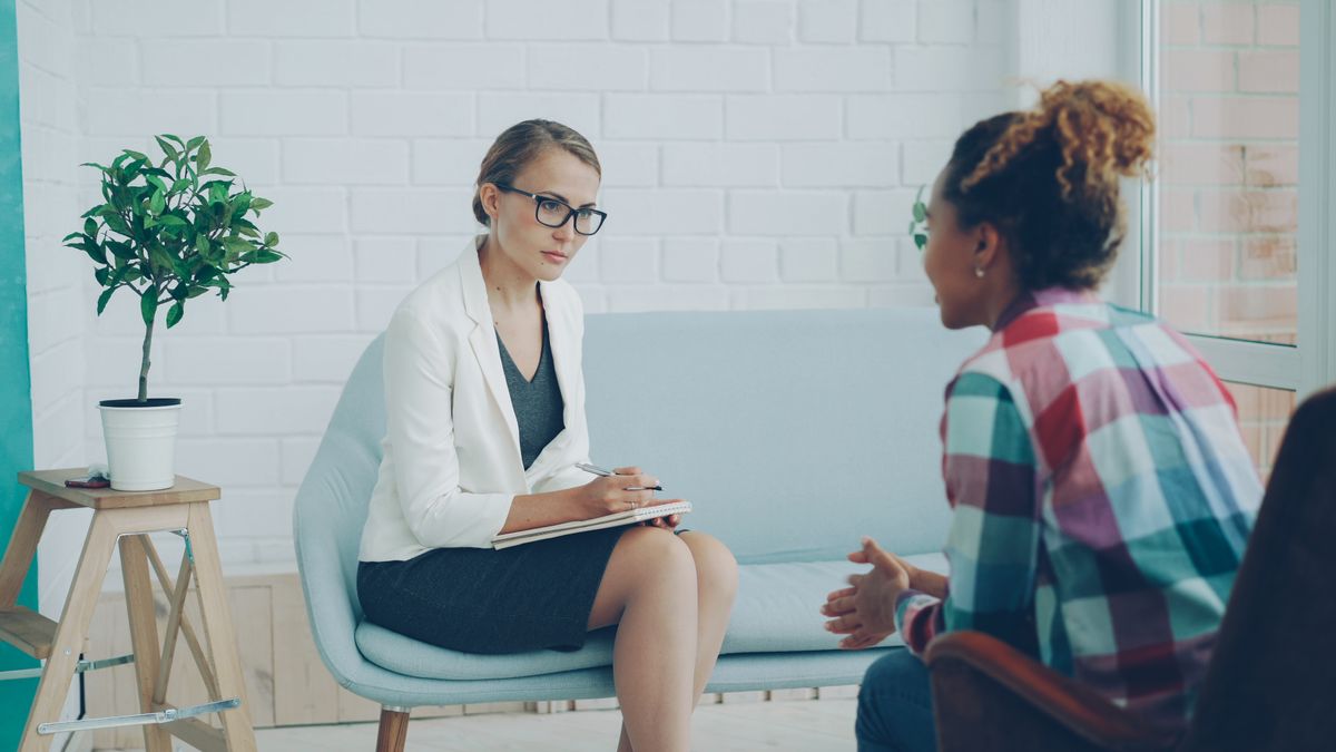 A practitioner taking notes while listening to a seated client.