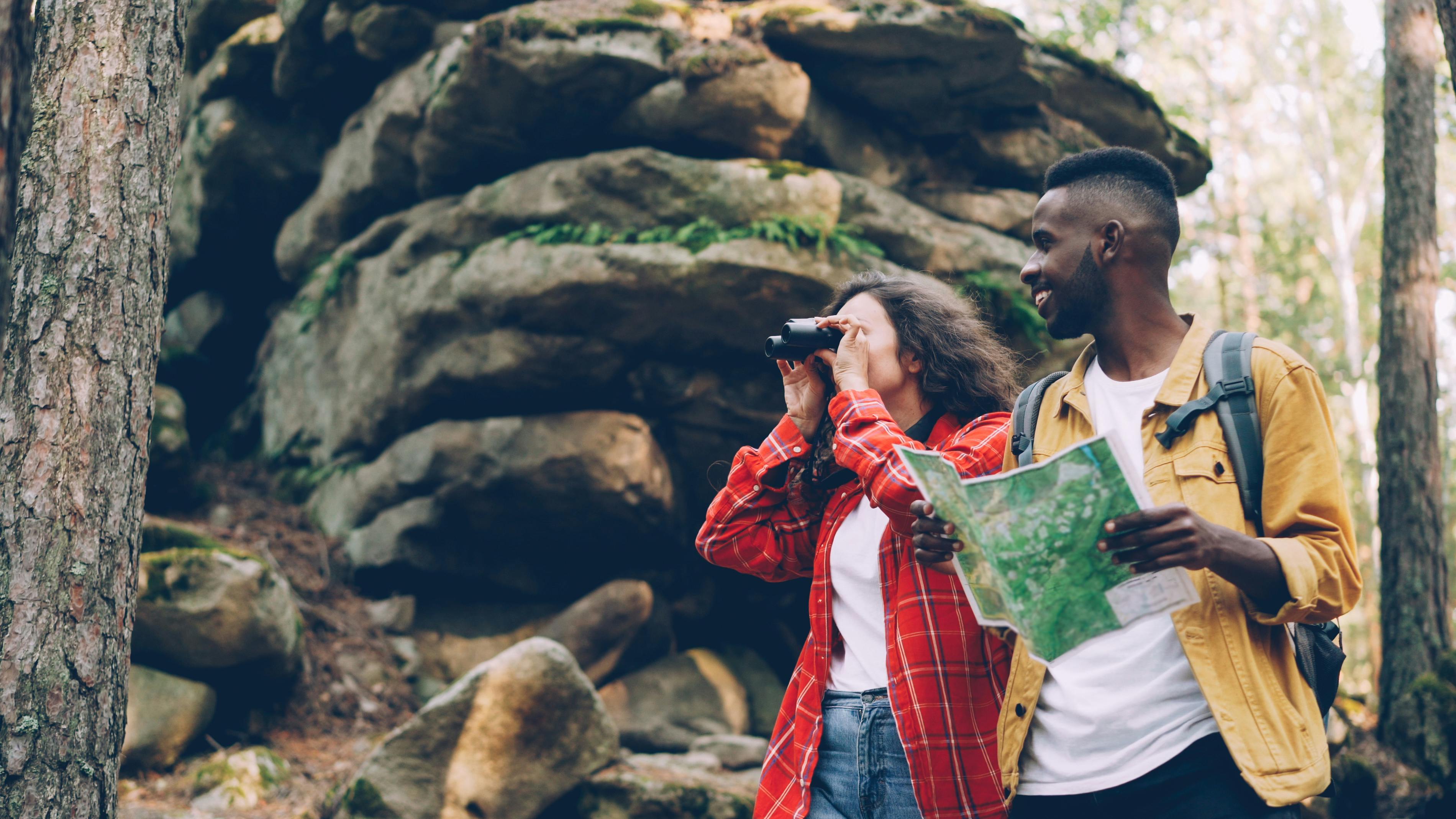 Two hikers exploring a forest with a map and binoculars, enjoying an outdoor adventure.