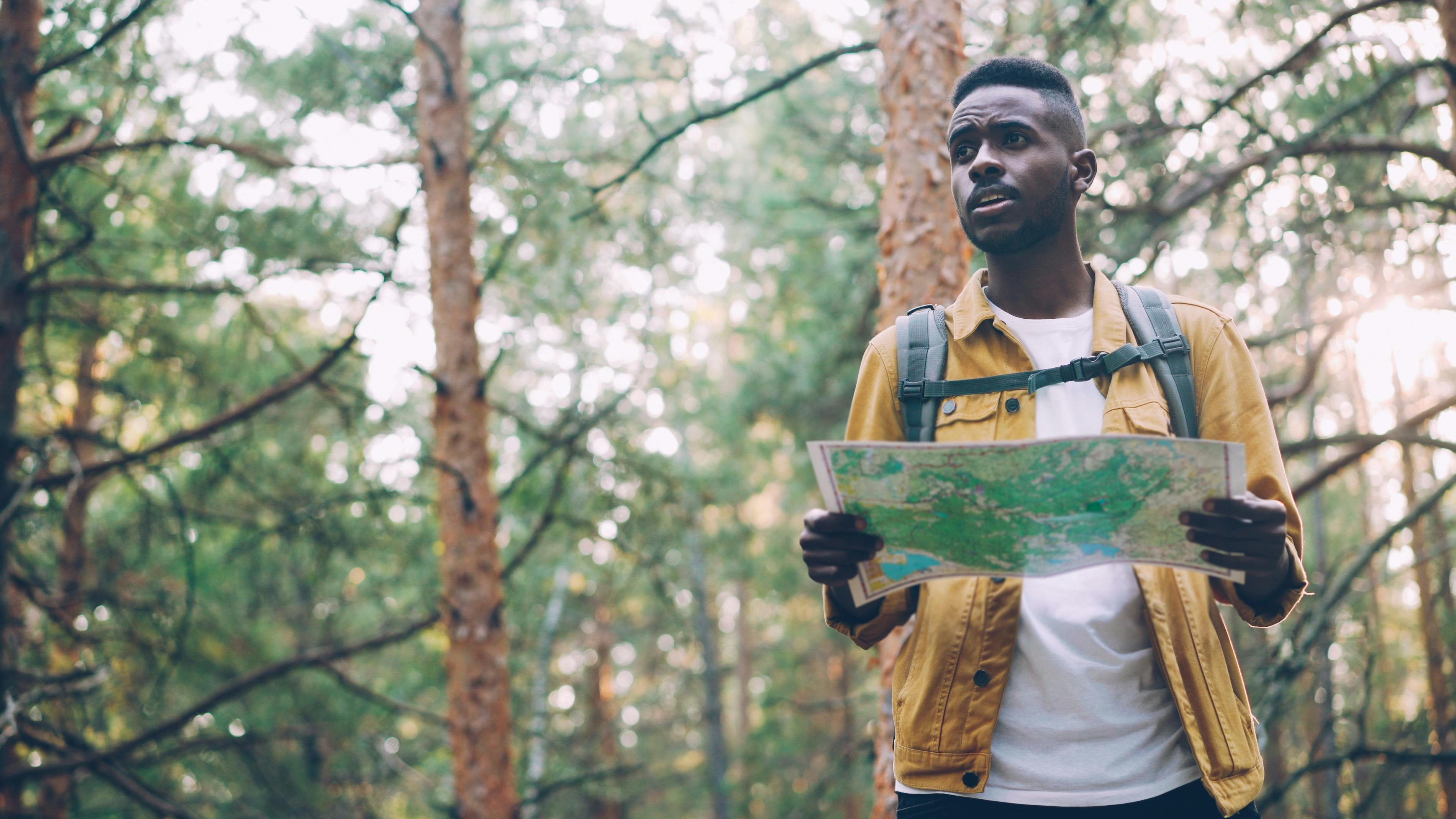 Young man with a backpack and map exploring a forest trail.