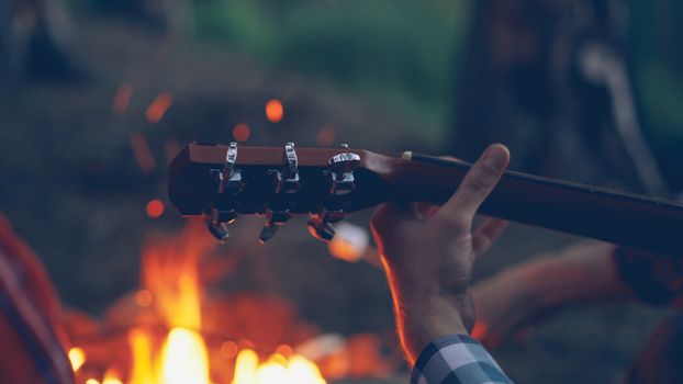 A person playing guitar by a campfire in the woods during twilight.
