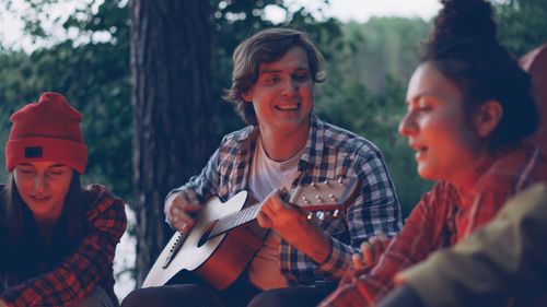 Free Group of friends playing guitar and singing by a campfire, enjoying an outdoor evening. Stock Photo
