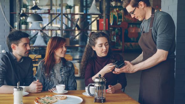 Friends paying the bill on a card terminal in a caf&eacute; &mdash; How to Split Costs on a Group Trip