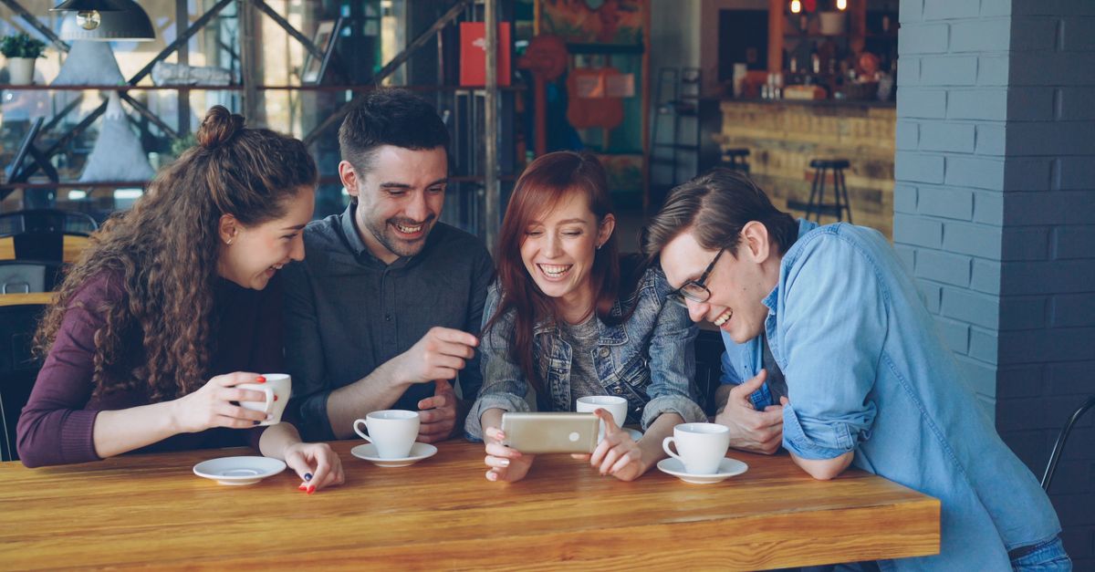 Four friends sharing a joyful moment over coffee in a trendy cafe.