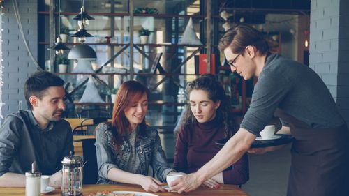 Free A barista serves coffee to friends at a cozy café. Warm and inviting scene. Stock Photo