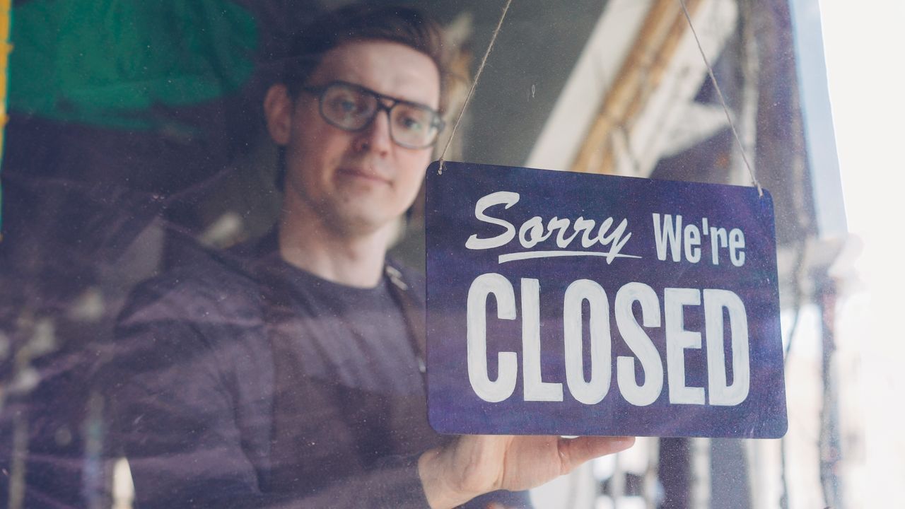 Shop owner holding a sorry we are closed sign in a store window