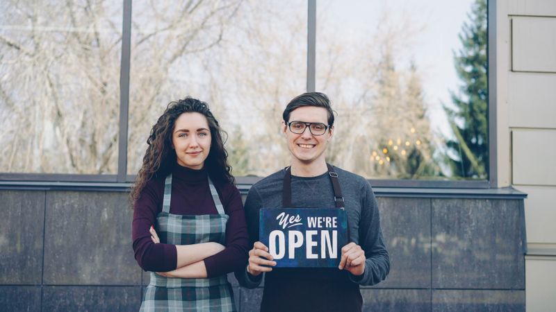 Local business owners displaying open sign welcoming community customers