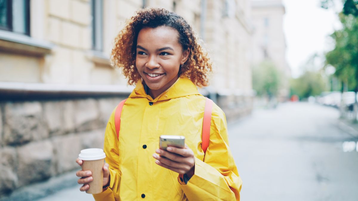 Traveller walking a city street with a coffee and a phone, photo by Vitaly Gariev on Pexels